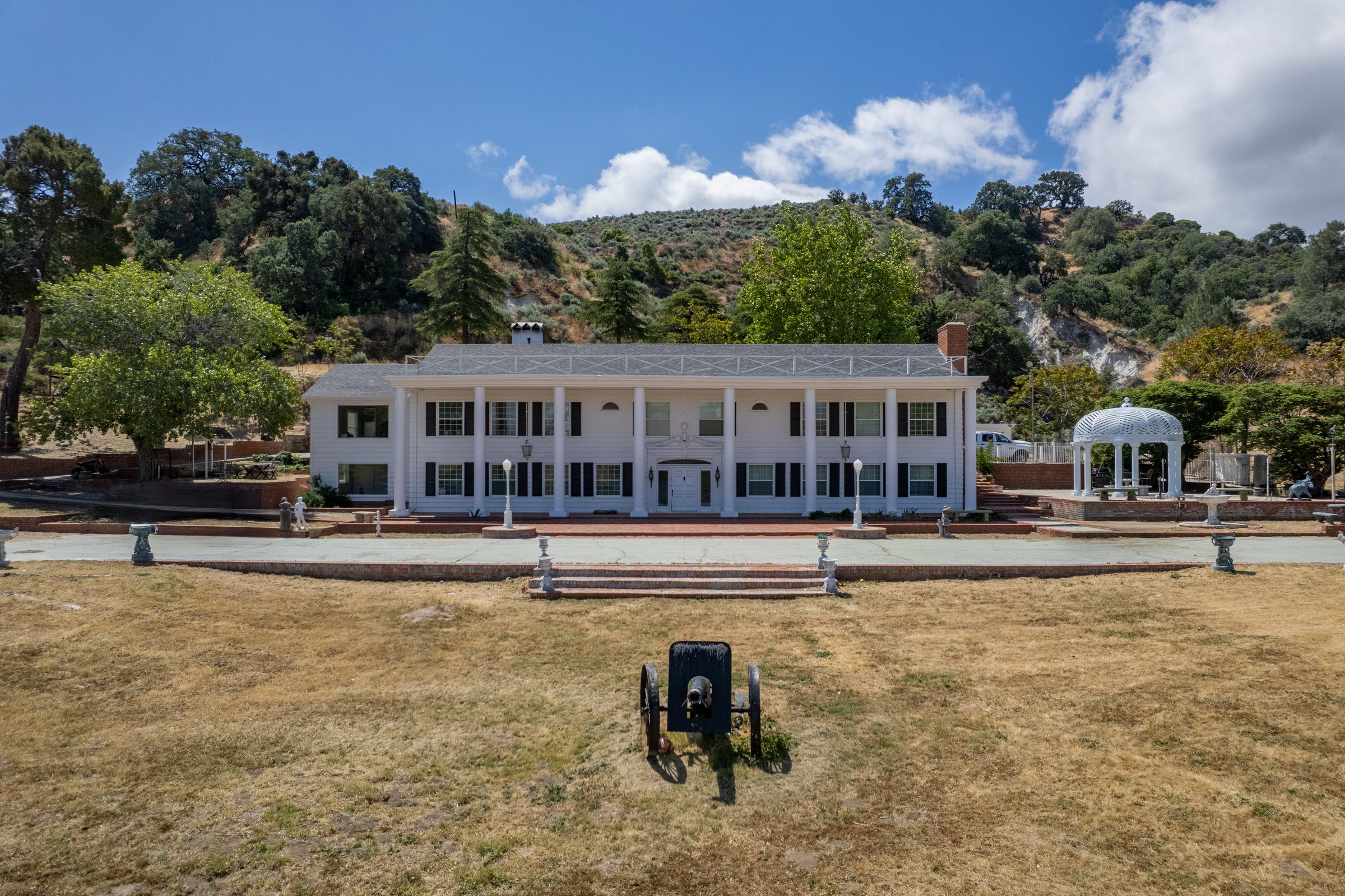 White colonial estate with a gazebo against oak-covered hills
