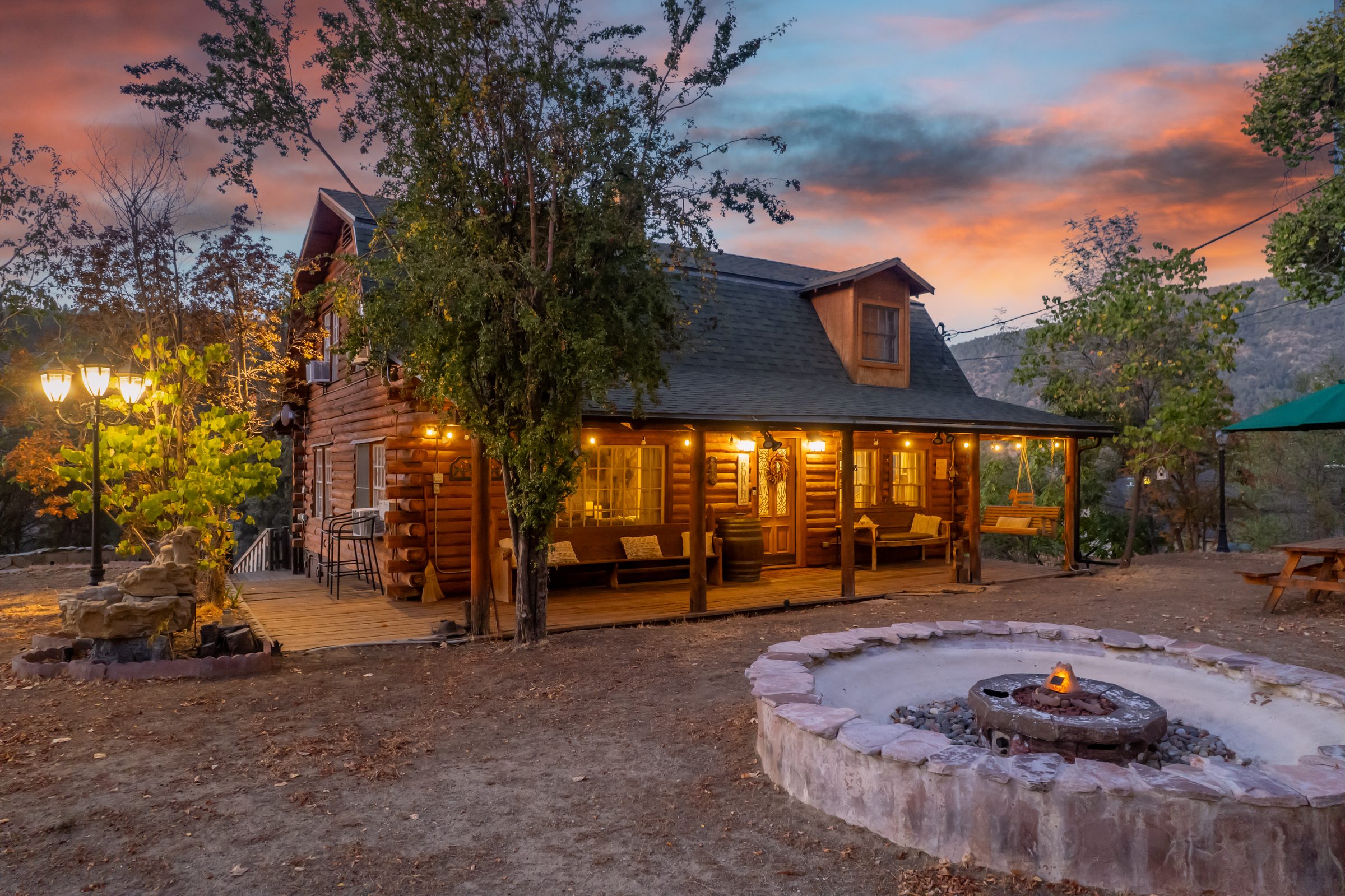 Log cabin glowing at twilight with a lit fire pit